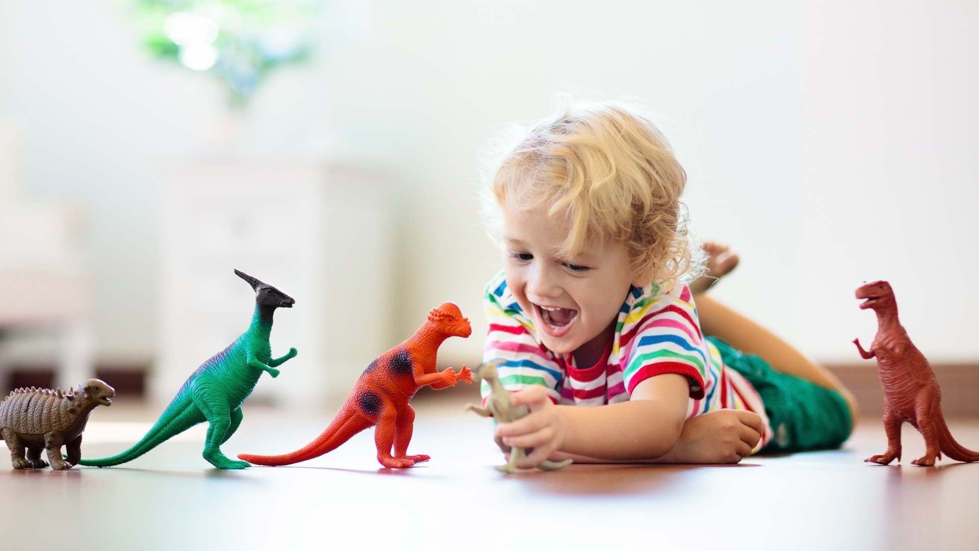 Child,Playing,With,Colorful,Toy,Dinosaurs.,Educational,Toys,For,Kids. Kind liegt auf dem Fußboden und spielt mit Dinos